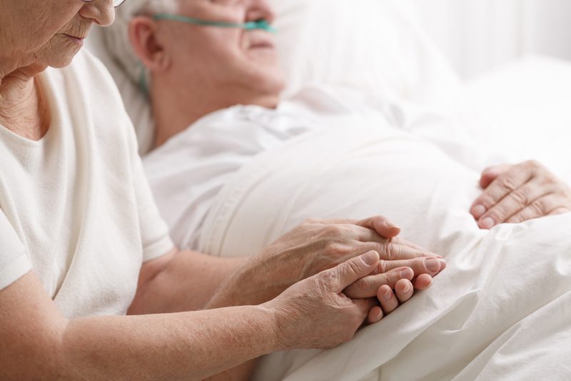 riverview-hospice-and-palliative-care-woman-holding-husband-hand Riverview Hospice and Palliative Care LLC | woman holding her ill husband's hand as he lays in bed